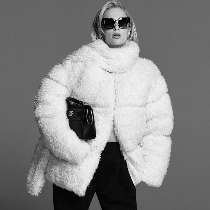 Person wearing a fluffy white coat and sunglasses against a gray background