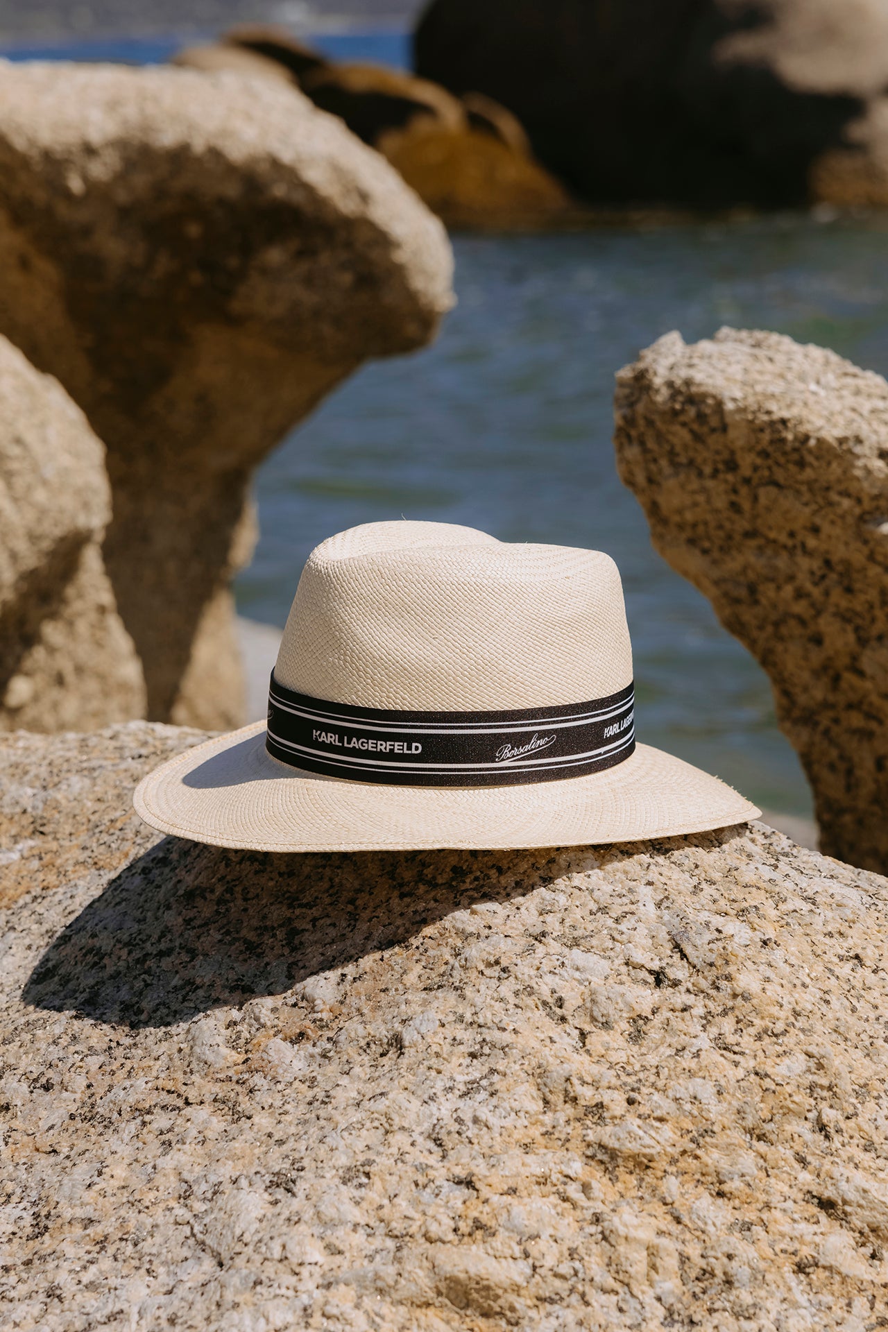 Beige hat with a black band on a rock by the water