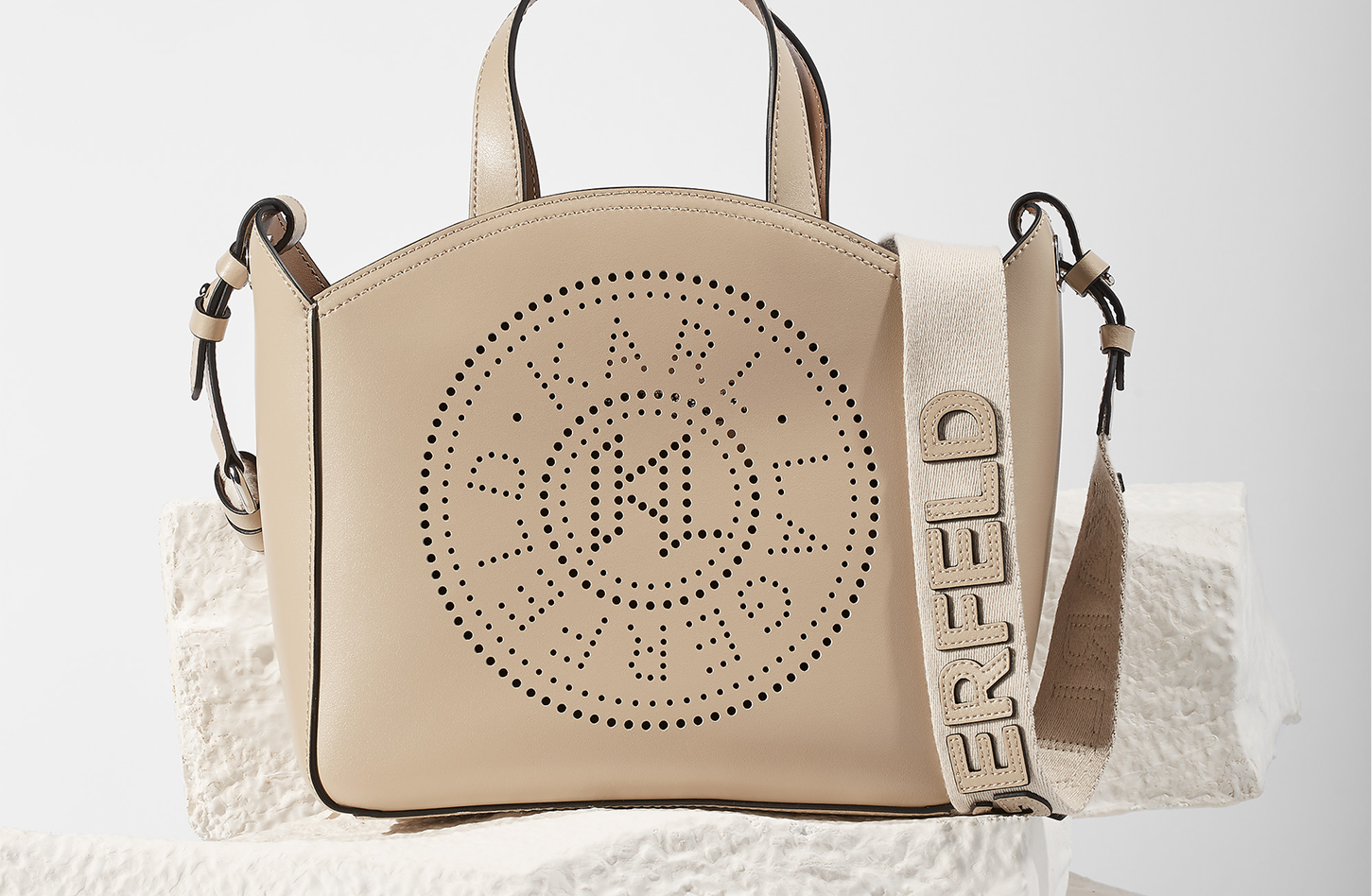 Beige handbag with brand logo and text on a textured white surface