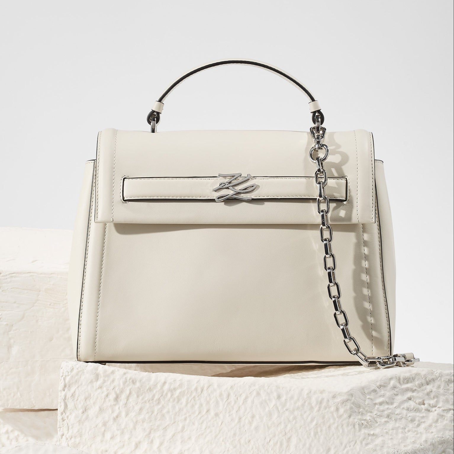 White handbag with a chain detail on a textured white surface