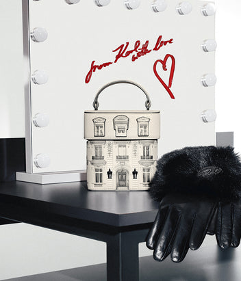 Small handbag with architectural design and black gloves on a black surface with a white background