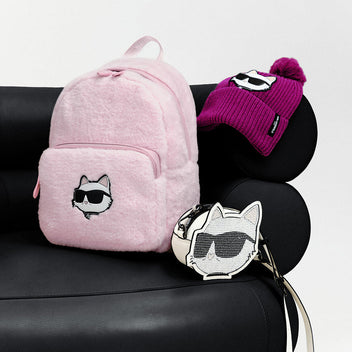 Pink backpack, purple beanie with pom-pom, and silver keychain with cat design on a black surface.