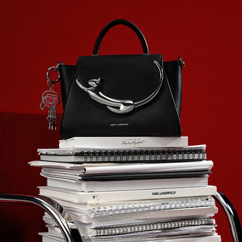 Black handbag with silver handle on a stack of books against a red background