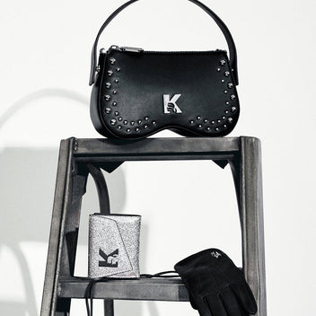 Black studded handbag, silver wallet, and black gloves on a wooden ladder against a white background.
