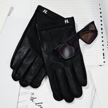 Black leather gloves and sunglasses on a light gray surface