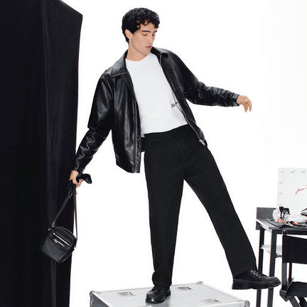 Man in black leather jacket and pants standing on a silver suitcase with a white background
