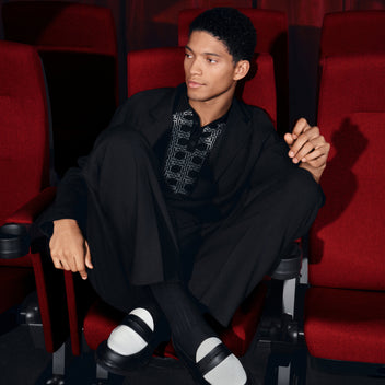 Man in a black suit sitting in a theater with red seats
