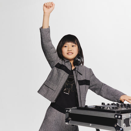 Child in a gray suit standing next to DJ equipment on a white background