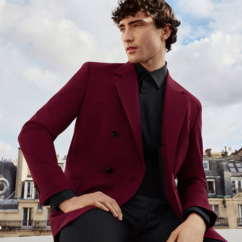 Man wearing a burgundy jacket over a black shirt with a cityscape background