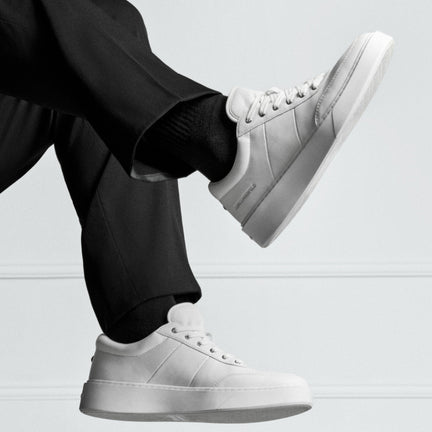 White sneakers worn with black pants on a light gray background