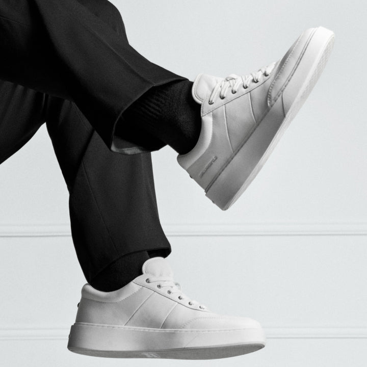 White sneakers worn with black pants on a light gray background