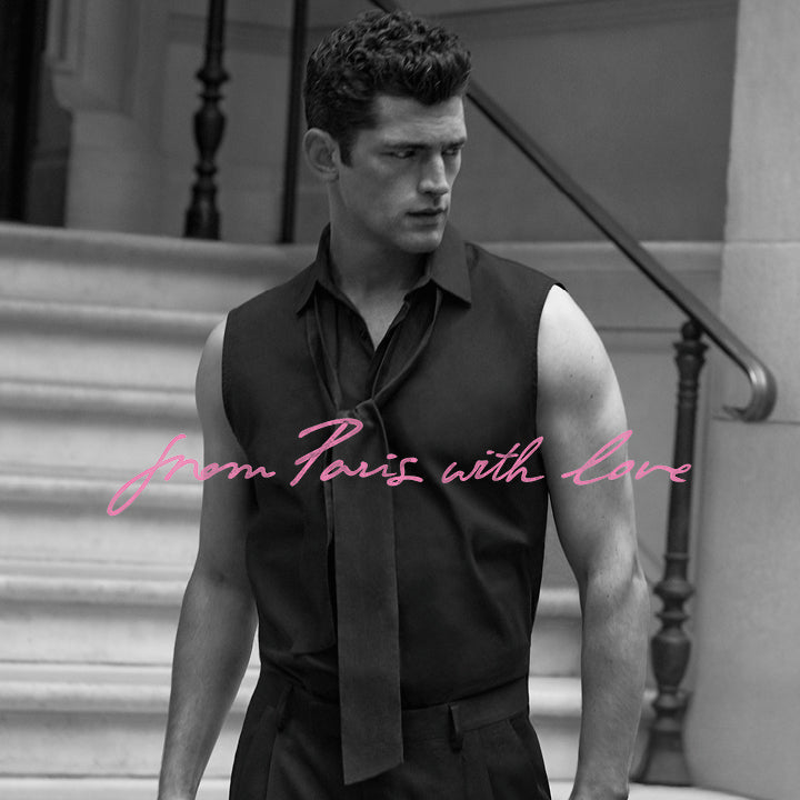 Man in a sleeveless black shirt with a tie standing on steps, text 'From Paris with Love' in pink.