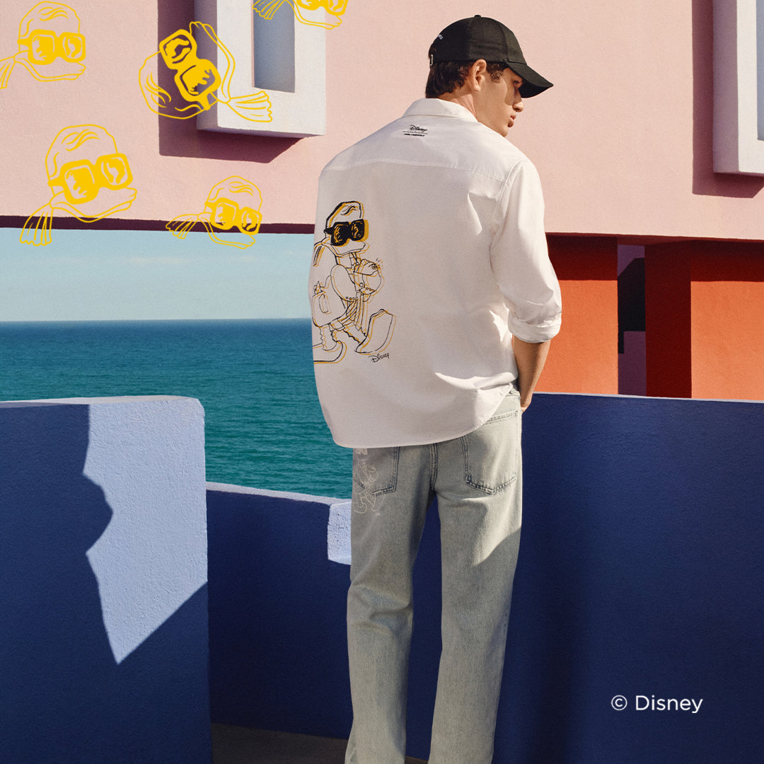 Person wearing a white shirt with a cartoon character on the back, standing in front of a colorful mural.