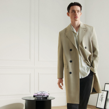 Man wearing a beige trench coat in a minimalistic room.