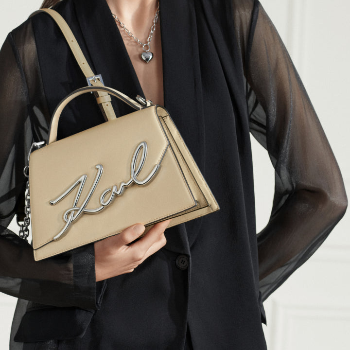 Beige handbag with 'Karl' embroidery held by a person wearing a black outfit.