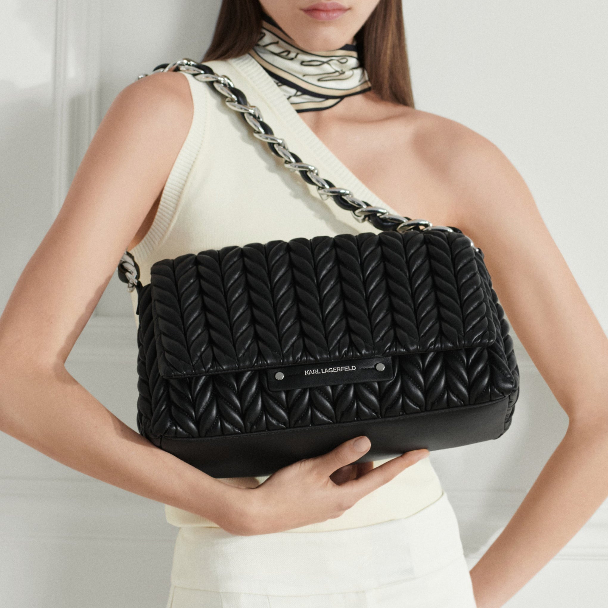 Woman holding a black quilted handbag against a white background