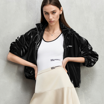 Woman wearing a black jacket, white top, and beige skirt against a gray background