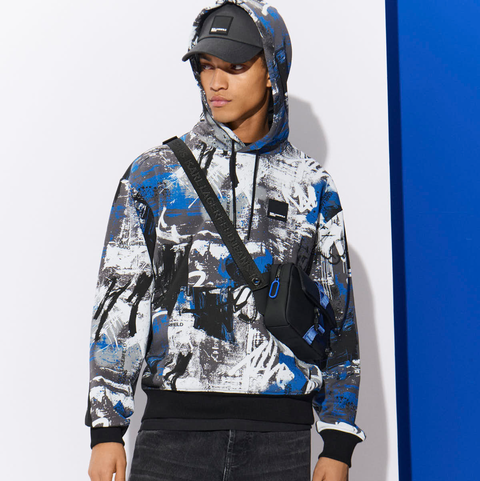 Person wearing a colorful hoodie with a black crossbody bag against a white and blue background