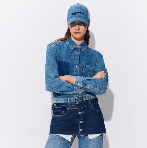 Person wearing a denim outfit with a jacket, skirt, and cap on a white background